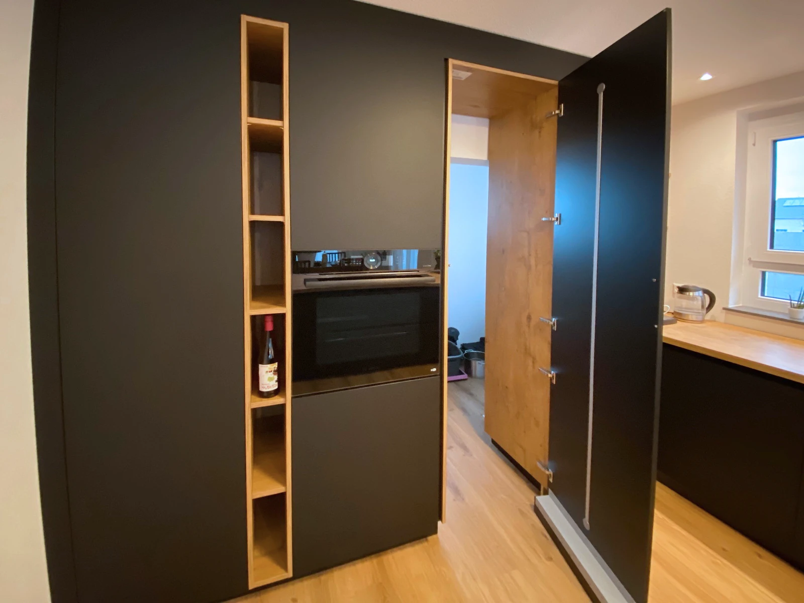 Mattschwarzer Hochschrank mit Einbaubackofen und schmalem Holzregal