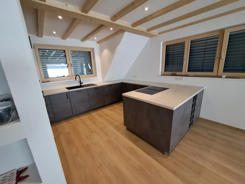Kücheninsel in Betonoptik Schiefergrau unter Holzbalken – Scholl Küchen Referenz